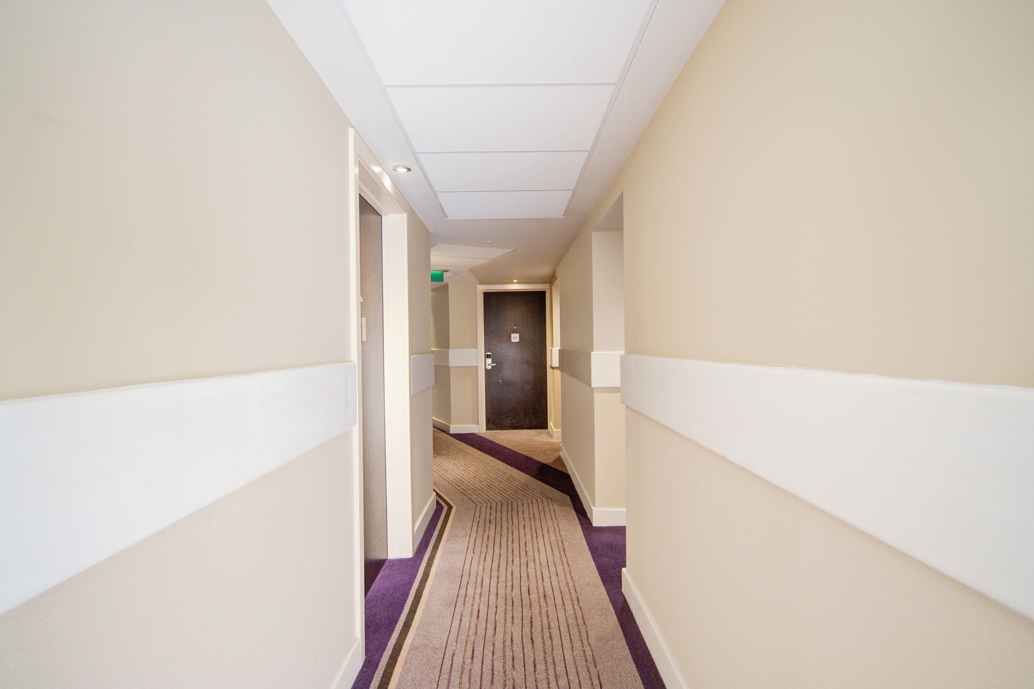 A narrow hotel corridor with a carpeted floor and white walls.