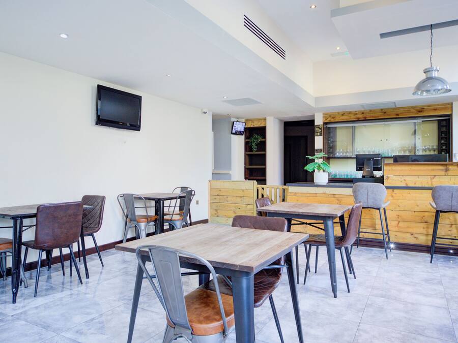 A modern restaurant interior with multiple tables and chairs, a wooden counter, and a flat-screen TV mounted on the wall.