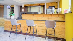 A reception area with a wooden counter, three grey bar stools, a potted plant, and a television mounted on the wall. - Belvilla Newport City Centre Hotel - Lifestyle (Newport)