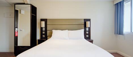 A large, neatly made bed with white linens in a hotel room.