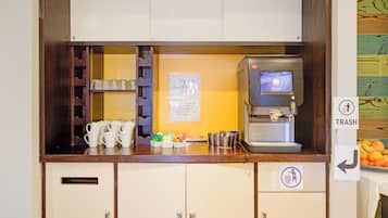 A coffee station with a coffee machine, cups, and a trash bin.