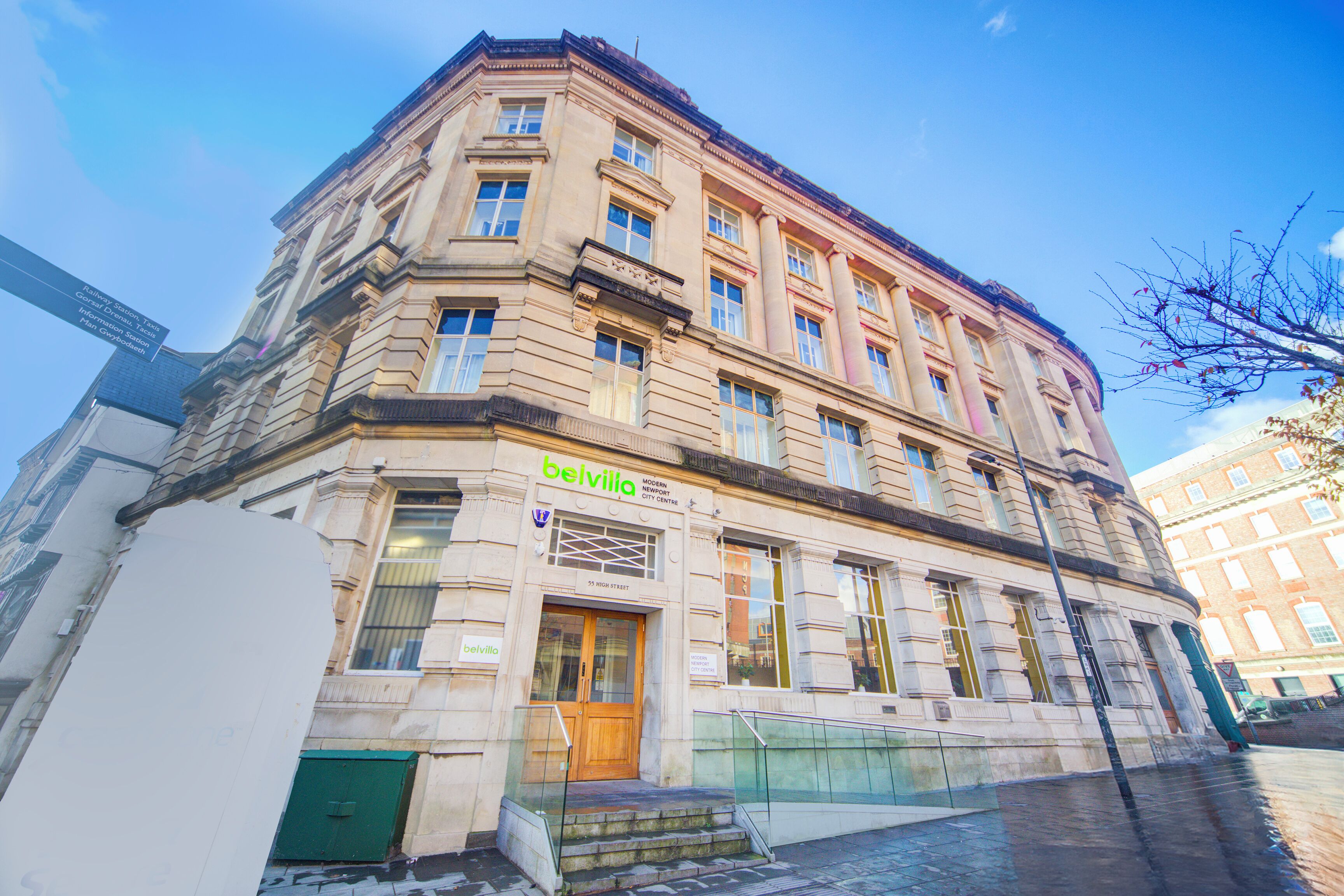 A historic building with a prominent entrance, large windows, and a sign reading "Belvilla."