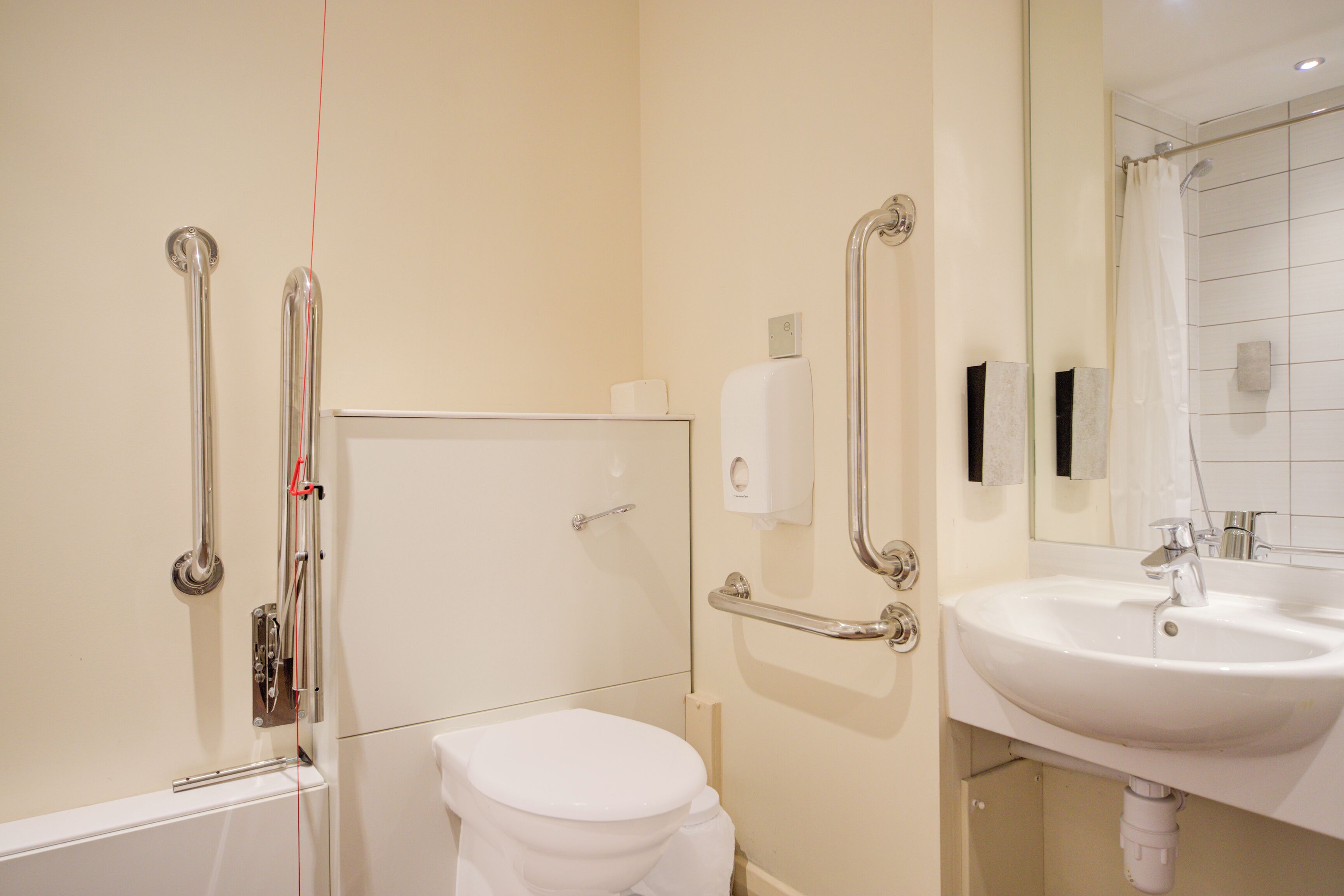 Un bany amb vàter blanc, un lavabo i una dutxa amb barres de sujeció.