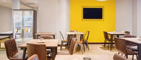 A dining area with multiple tables and chairs, a yellow accent wall, and a refrigerator in the background.