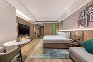 A hotel room with a bed, a TV, a desk, a chair, and a couch.