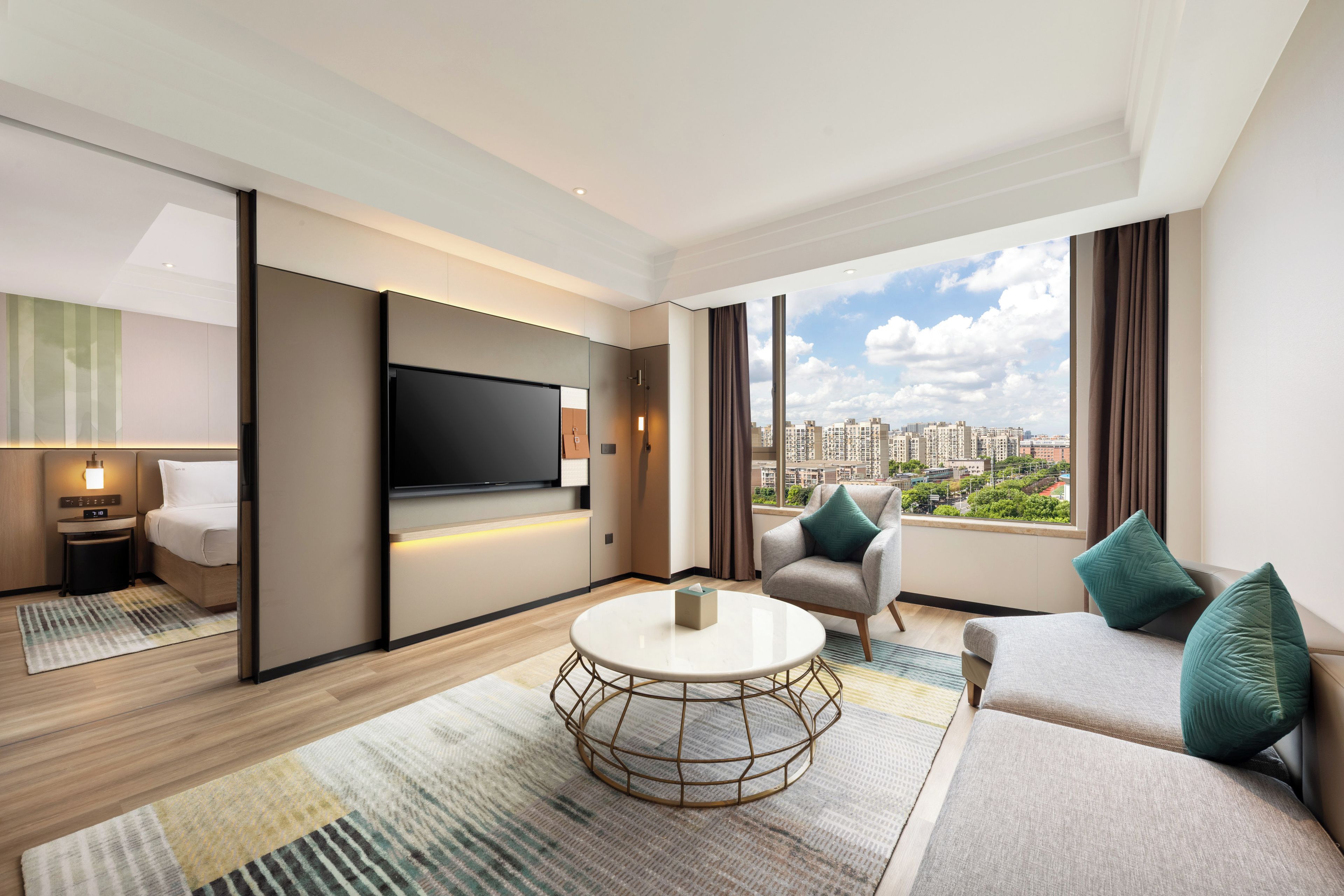 Een moderne hotelkamer met een flatscreen televisie, een bank, een ronde salontafel en uitzicht op de stad.