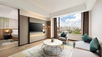 Een moderne hotelkamer met een flatscreen televisie, een bank, een ronde salontafel en uitzicht op de stad.