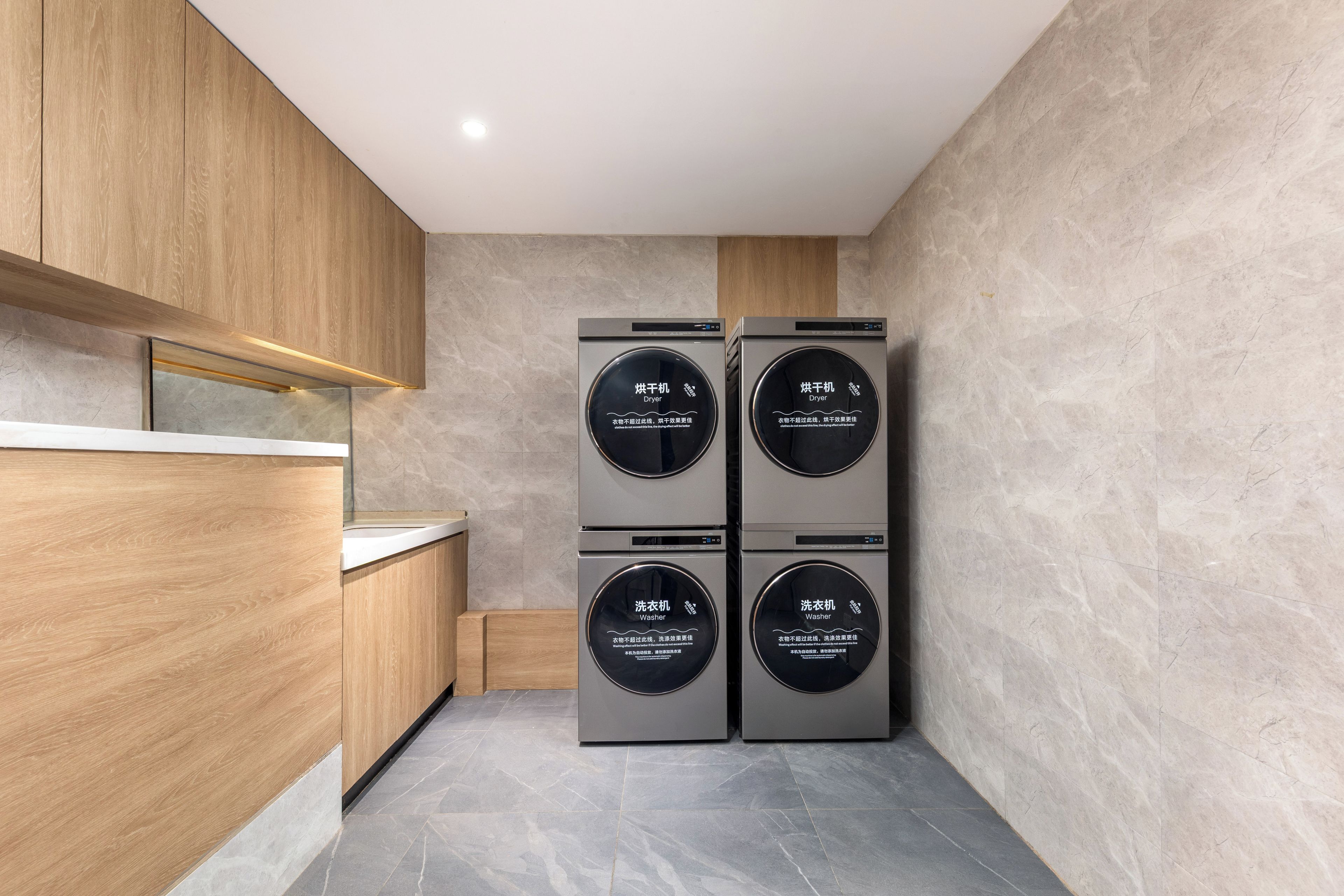 Une cuisine compacte dotée de meubles en bois, d’un plan de travail et de quatre appareils électroménagers : deux sèche-linge et deux machines à laver.
