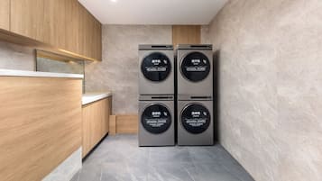 A compact kitchen with wooden cabinetry, a countertop, and four appliances: two dryers and two washers.