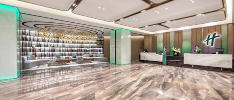 Een moderne hotellobby met een receptiebalie, een zithoek en een decoratief plafond.