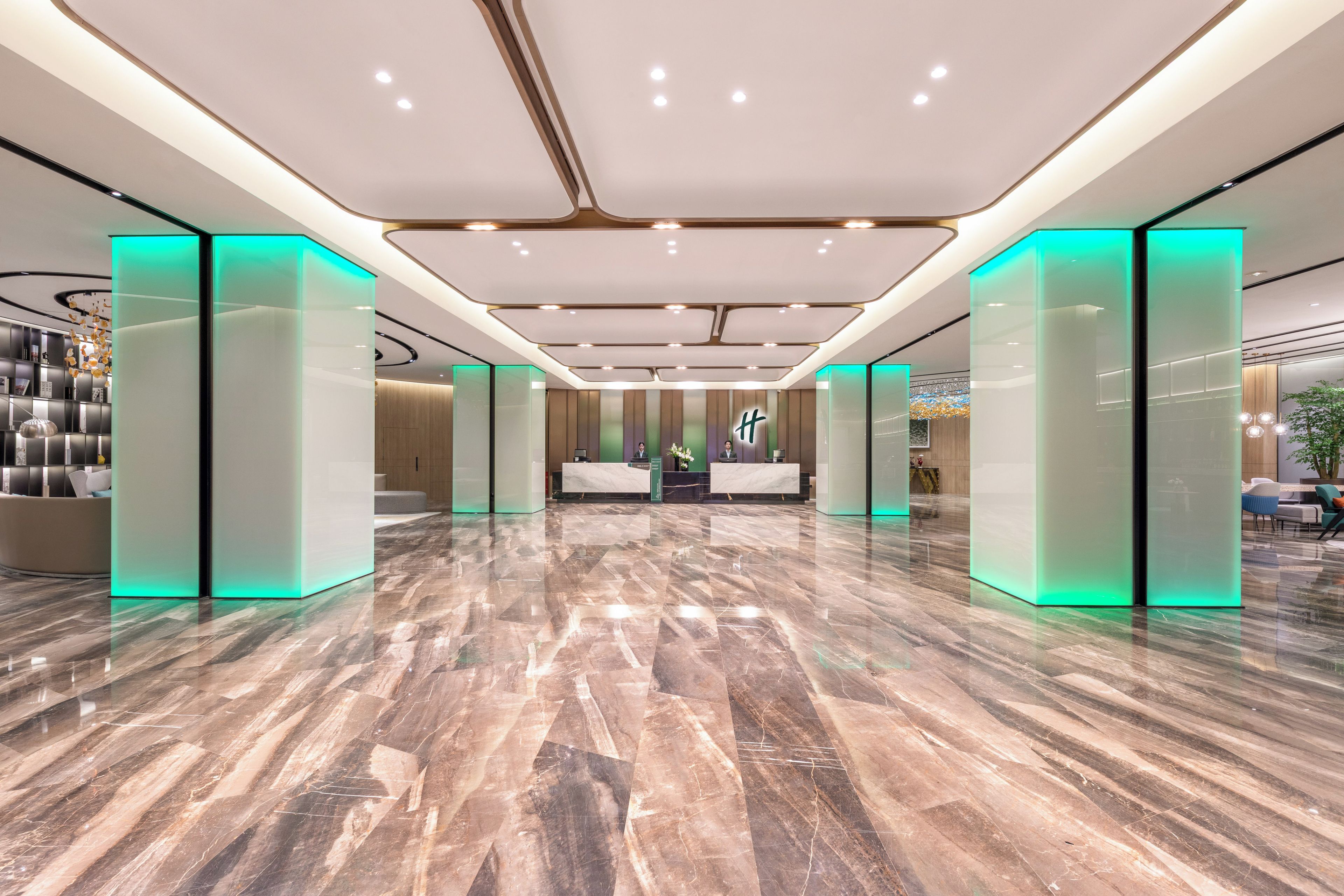 Un vestíbulo amplio con suelo de mármol, un mostrador de recepción y separadores de vidrio con iluminación verde.