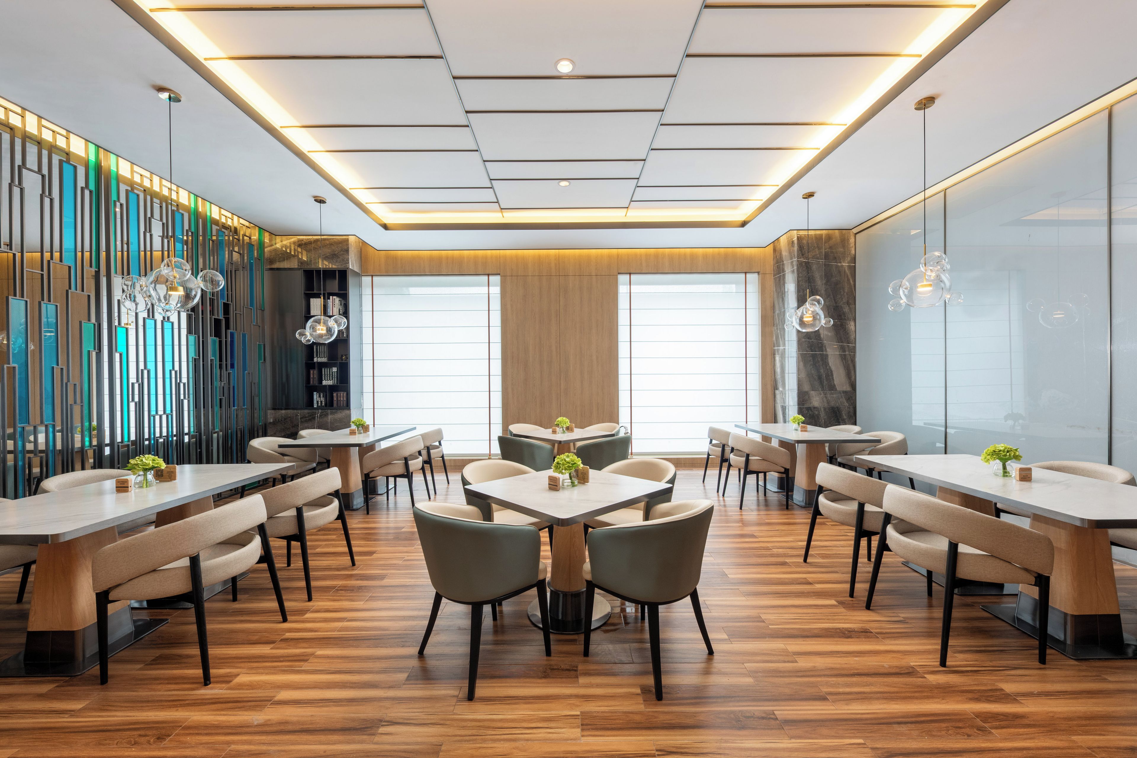 Un comedor moderno con varias mesas y sillas, una pared decorativa con paneles verticales e iluminación empotrada en el techo.