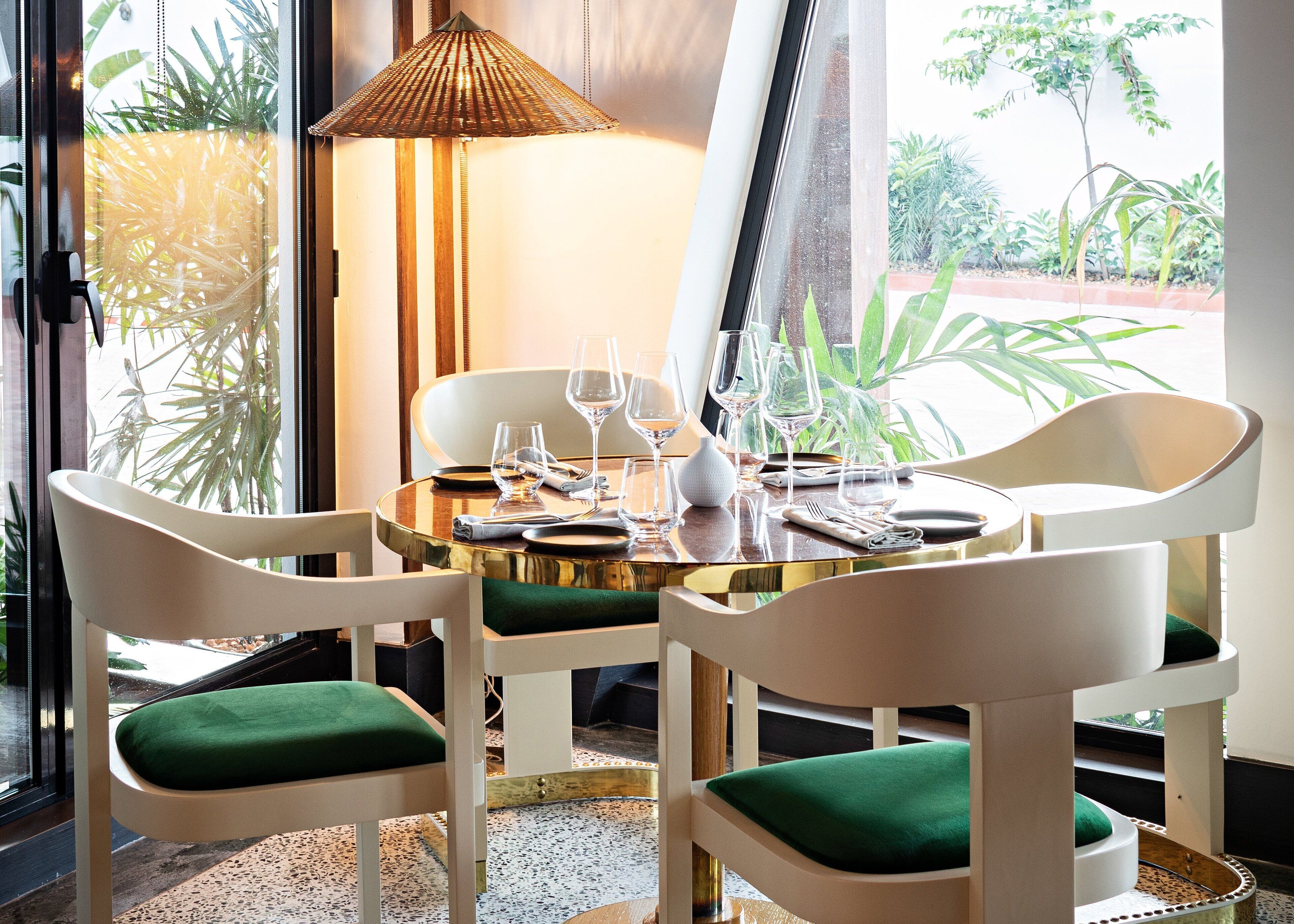A dining area with a round table, white chairs with green cushions, and a hanging lamp.