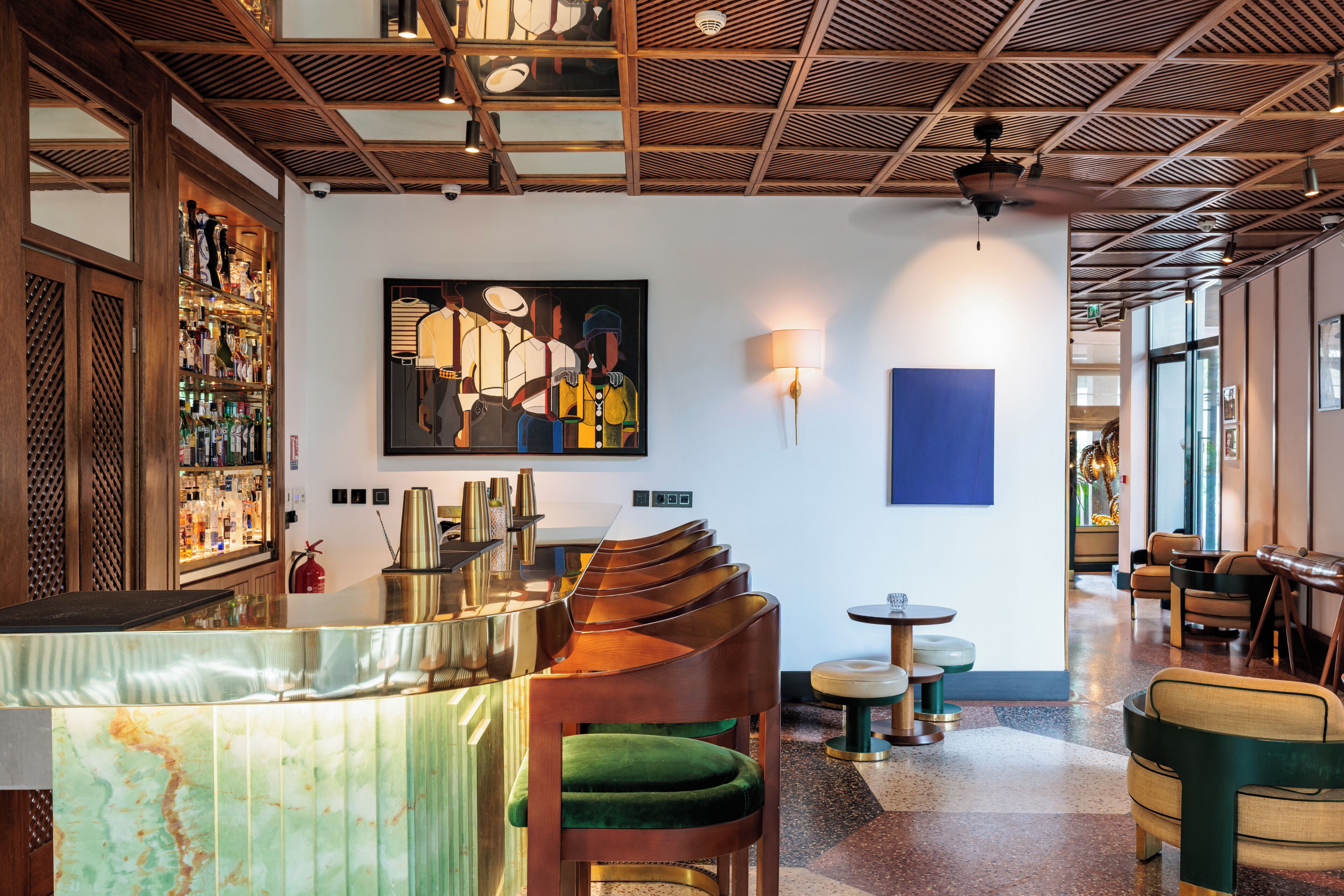A bar area with a wooden counter, green cushioned chairs, and a large abstract painting on the wall.