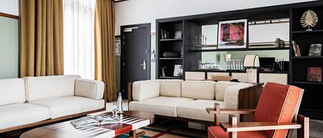 Una sala de estar moderna con un sofá, una mesa de centro y un sillón rojo. Se observa una estantería con libros y objetos decorativos.