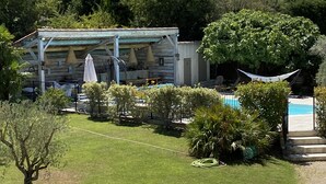 A rustic outdoor seating area with a wooden pergola, a pool, and lush greenery. - Superb 250 m2 Provencal farmhouse for rent (Mas-Blanc-des-Alpilles)