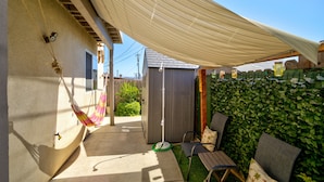 Ein überdachter Patio-Bereich mit einer Hängematte, einer Holzbank und einer grünen Wand.