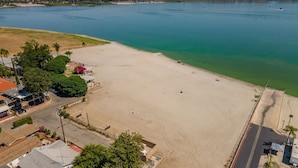Ein weitläufiges, offenes Sandstrandgebiet neben einem Gewässer, mit einigen Gebäuden und Bäumen in der Nähe.