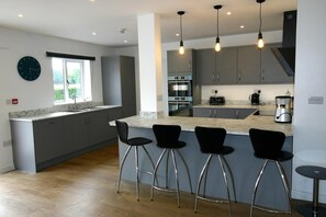 Una cucina moderna con mobili grigi, un piano di lavoro in marmo e forno integrato. Sono presenti quattro sgabelli neri e un tavolo rotondo.