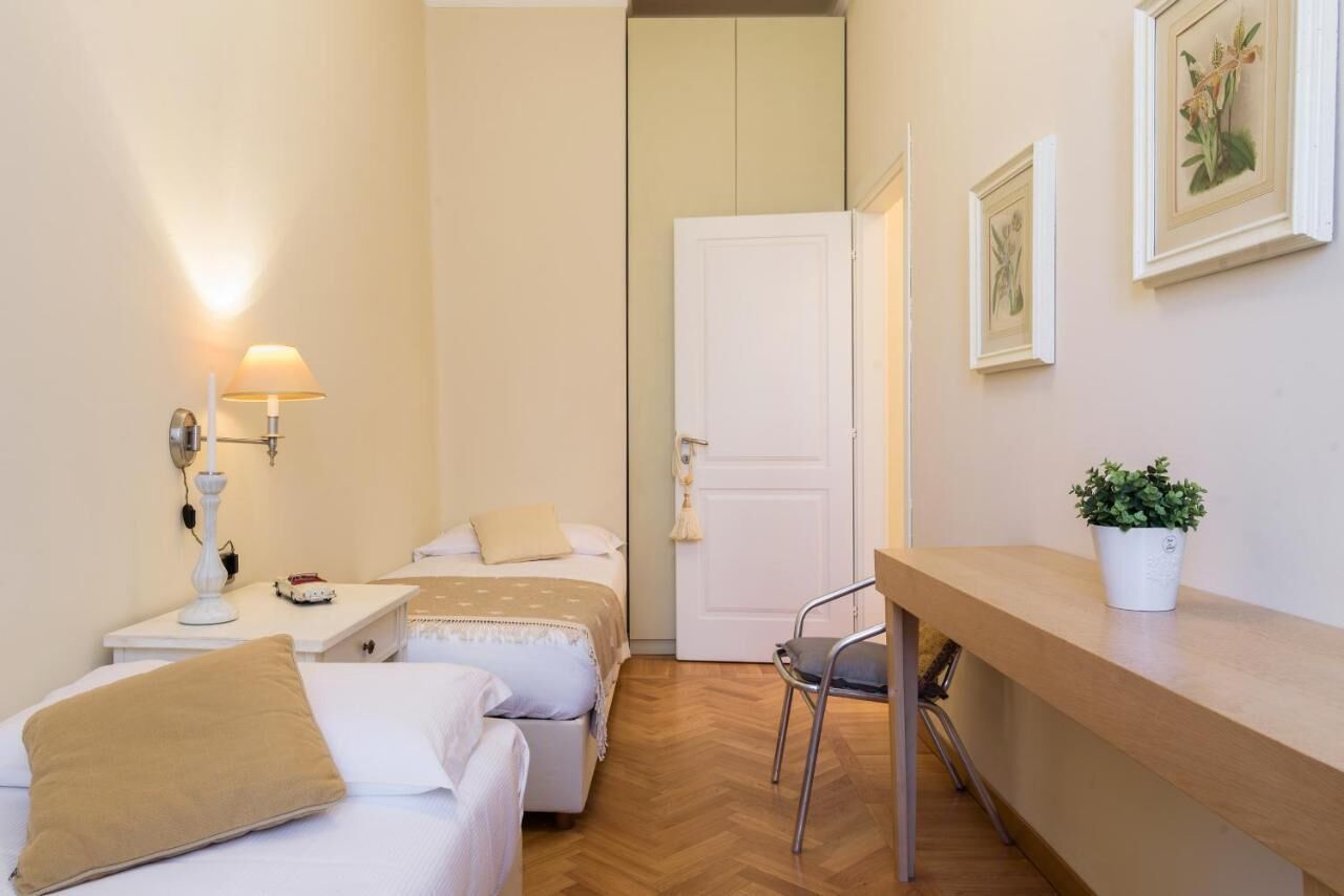 A small, clean room with two beds, a desk, a chair, a lamp, and a potted plant.