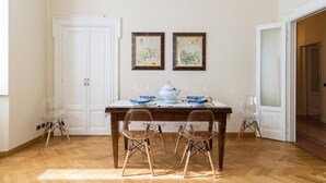 En matplats med ett träbord dukat för fyra personer, två stolar, en vit dörr och två inramade konstverk på väggen.