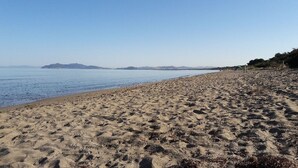 Une vaste plage de sable offrant une vue dégagée sur la mer et les collines lointaines.
