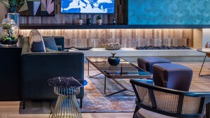 A modern living room with a large flat-screen TV, a sofa, a coffee table, and a patterned wall. - TITANIC Comfort Kurfürstendamm (Berlin)