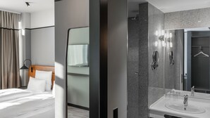 A modern hotel room with a neatly made bed, a large mirror, a bathroom with a sink and a shower. - TITANIC Comfort Kurfürstendamm (Berlin)