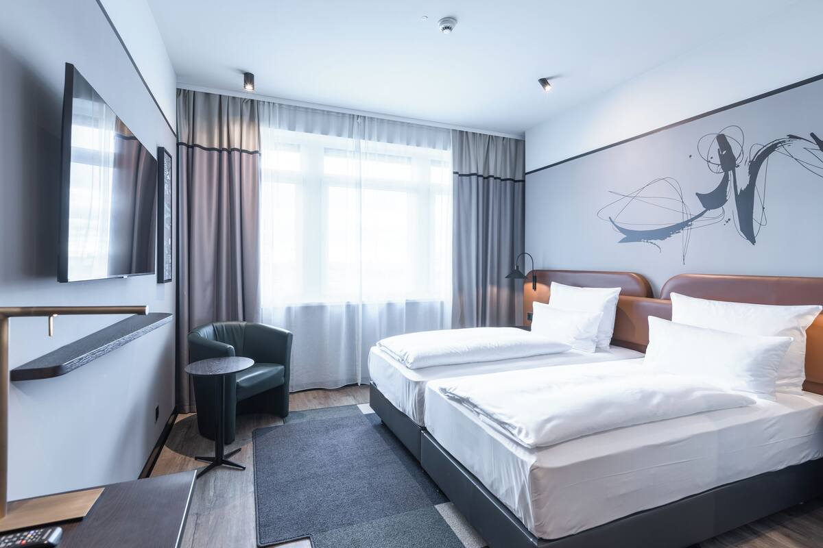 A modern hotel room with a large bed, a desk, a chair, and a TV.
