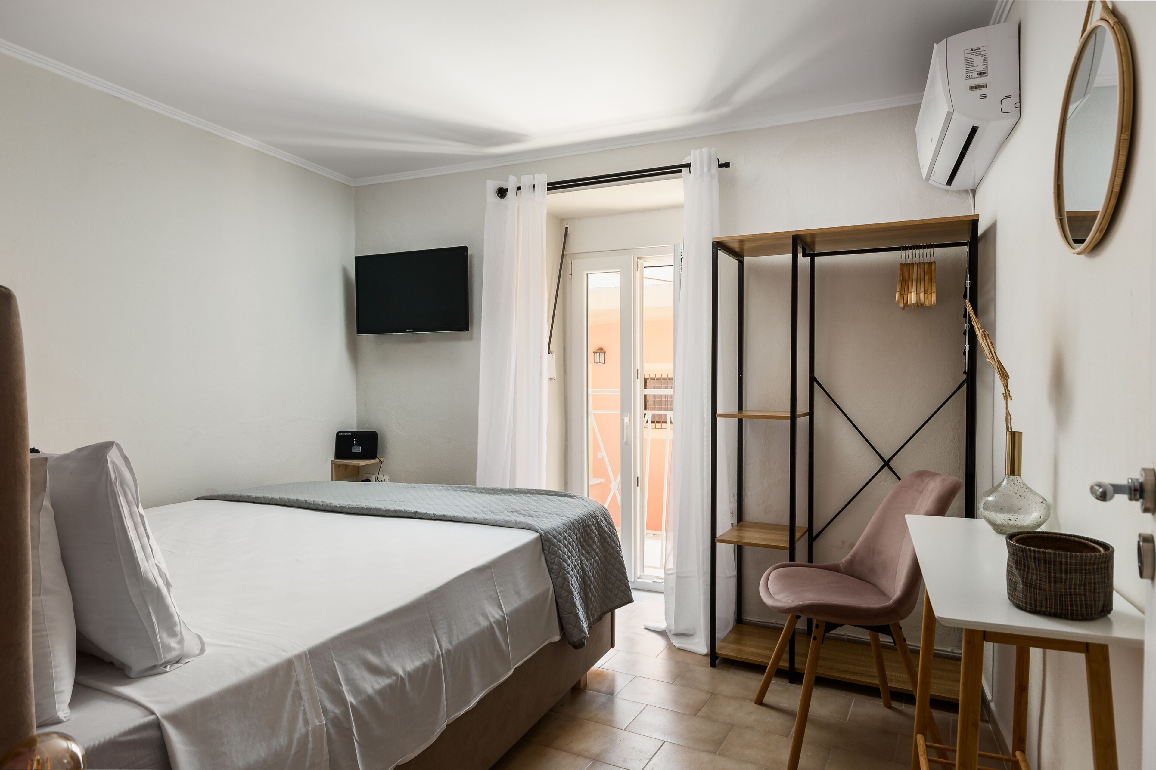 Ein Schlafzimmer mit Bett, Fernseher, Schreibtisch mit Stuhl, Kleiderschrank und Balkontür.