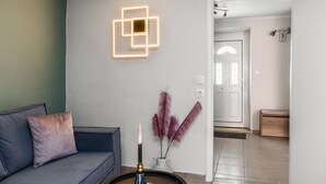 A modern living room with a grey sofa, a decorative wall piece, and a vase with feathers. - Armonia GuestHouses by Konnect, Benitses (Corfu)