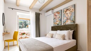 A bedroom with a bed, a chair, a balcony with a table and chairs, and two paintings on the wall. - Armonia GuestHouses by Konnect, Benitses (Corfu)