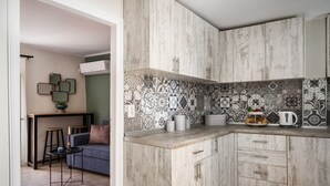A modern kitchen with wooden cabinets, a tiled backsplash, and a dining area with a sofa and stools. - Armonia GuestHouses by Konnect, Benitses (Corfu)