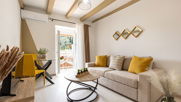 A modern living room with a sofa, a round coffee table, and a dining area with chairs and a table. - Armonia GuestHouses by Konnect, Benitses (Corfu)