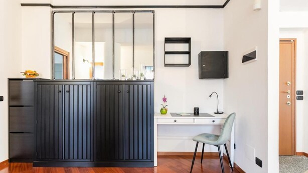 A room with a black cabinet, a white desk, a chair, and a large mirror. - MyHomeInComo - Santa Chiara Apartment (Como)