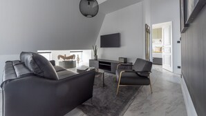 A modern living room with a black leather sofa, a grey armchair, a coffee table, and a TV mounted on the wall. - Seaham, 4 stars, View on Eiffel Tower and Sacré-Coeur (París)