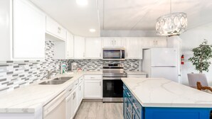 A modern kitchen with white cabinets, a blue island, stainless steel appliances, and a patterned backsplash.