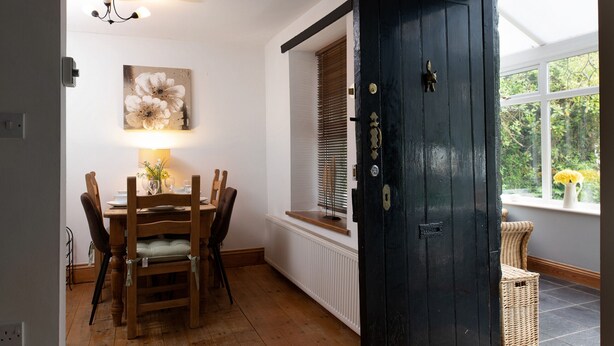 A dining area with a wooden table and chairs, a wall-mounted lamp, and a window with blinds.