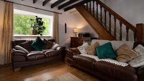 A living room with two brown leather sofas, a wooden staircase, and a large window with curtains.