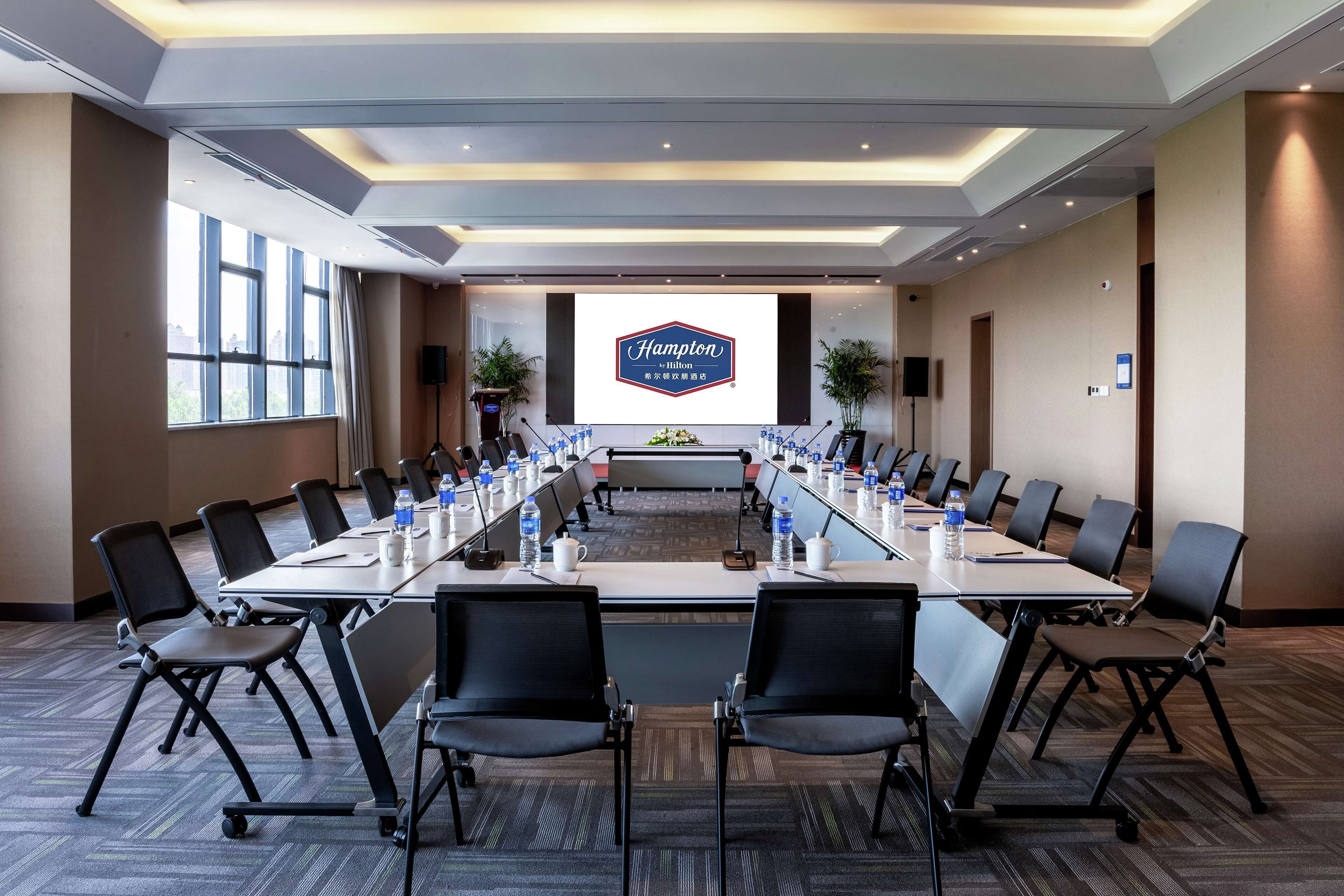 A conference room with a long table, multiple chairs, and a large screen displaying the Hampton Inn logo.