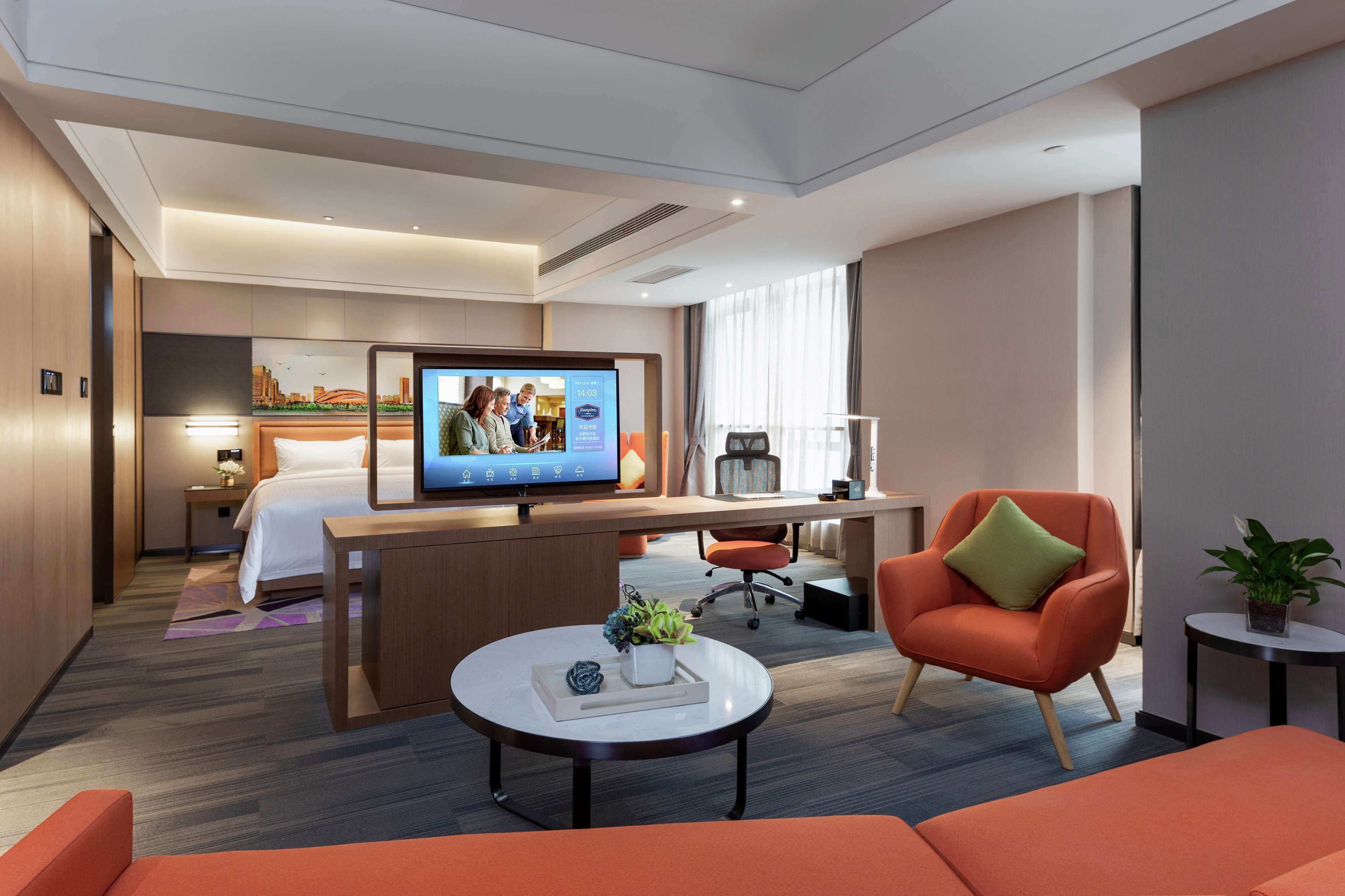 A modern hotel room with a bed, desk, chair, and television.
