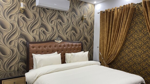 Une chambre avec une tête de lit capitonnée, un lit avec une literie blanche, un climatiseur fixé au mur et des rideaux à motifs.