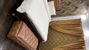 Une chambre à coucher bien aménagée, avec un lit, un pouf en cuir marron, un tapis à motifs et une tête de lit décorative.