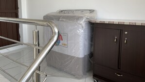 Une pièce dont le sol est recouvert de carreaux de marbre, un meuble en bois foncé avec deux tiroirs, et un matelas enveloppé dans du plastique.