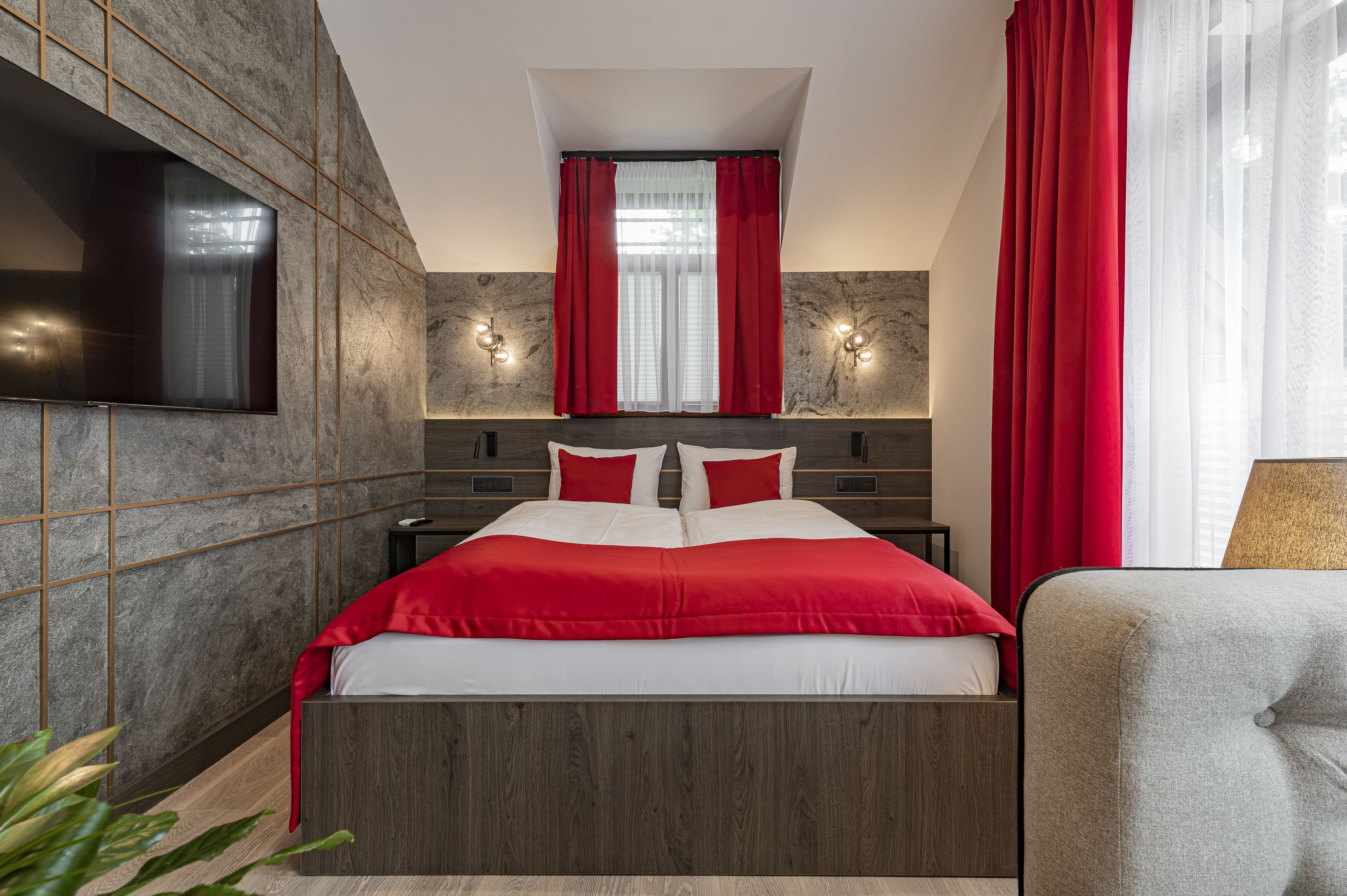 A modern bedroom with a large bed, red curtains, a TV mounted on the wall, and a small table beside the bed.