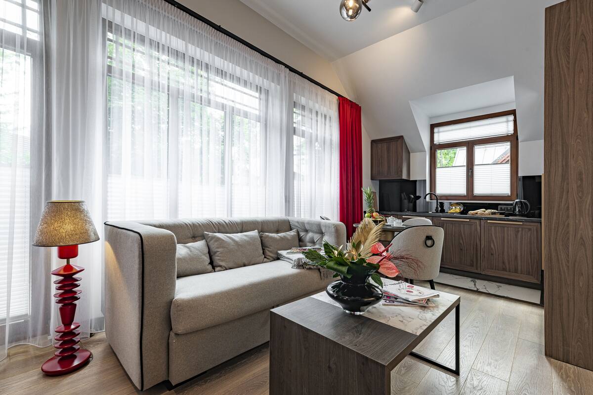 A modern living room with a sofa, a coffee table with a vase, and a kitchen in the background.