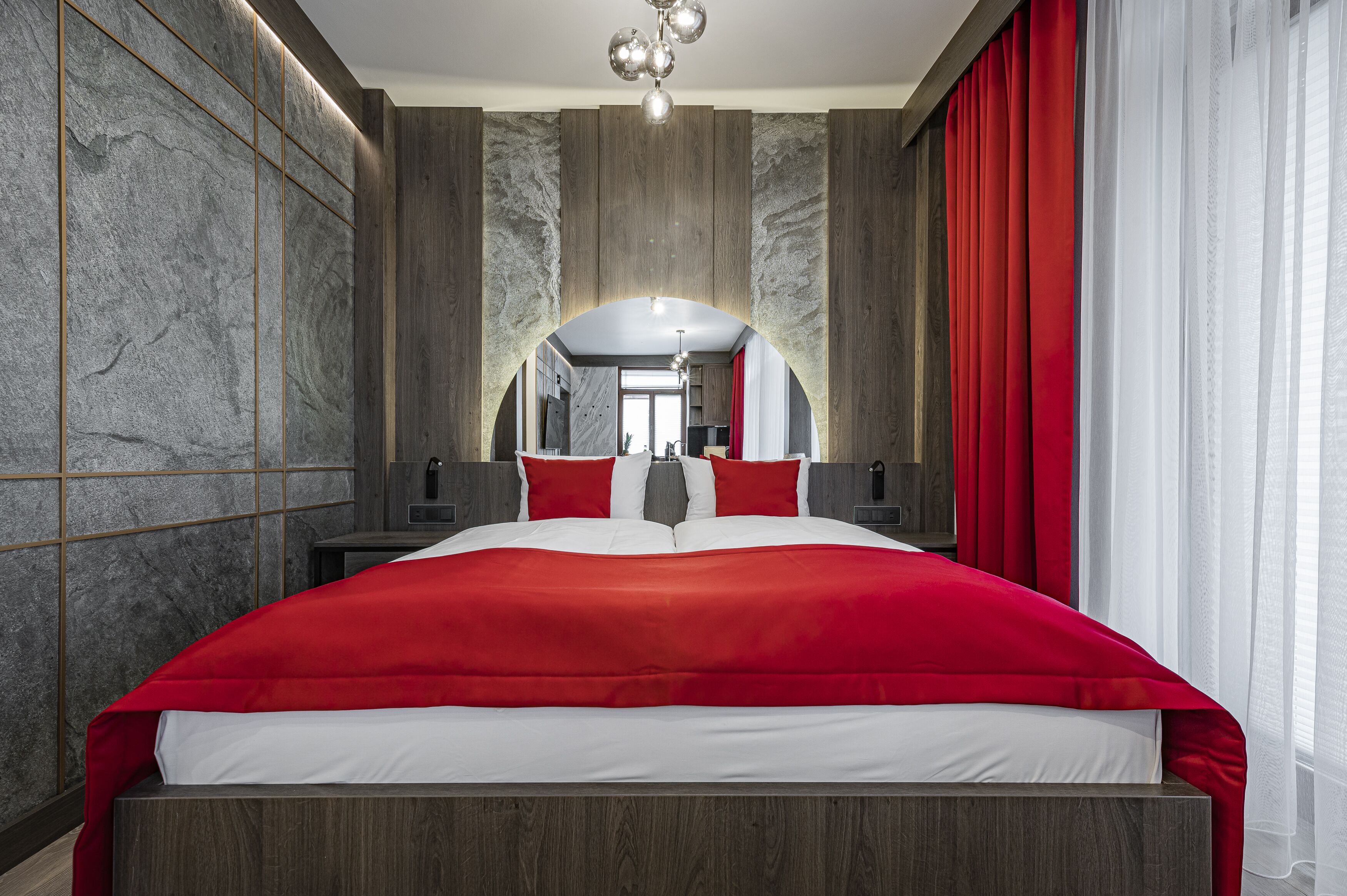 Ett modernt hotellrum med en stor säng, väggar i marmor och en röd gardin.