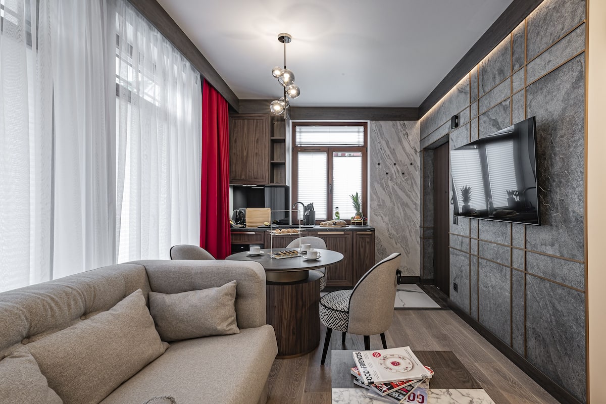 A modern living room with a sofa, a dining table, and a TV mounted on the wall.