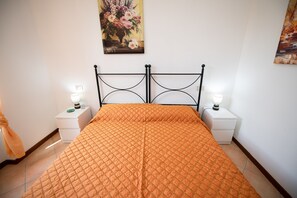 A bedroom with a bed, two bedside tables with lamps, a painting on the wall, and a curtain on the left.