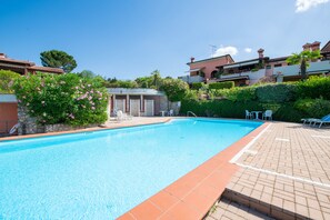 A swimming pool with a tiled edge, surrounded by greenery and a few lounge chairs.